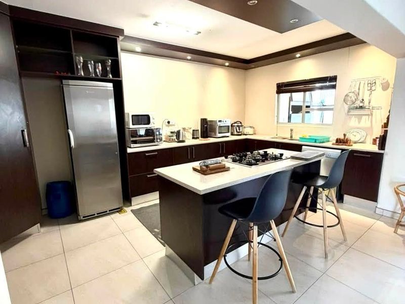 Modern kitchen featuring a central island with a gas cooktop, dark wood cabinetry, recessed ceiling lighting, and light-toned tiled flooring.