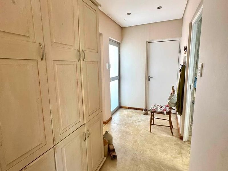 A functional hallway featuring extensive built-in cabinetry for storage, recessed ceiling lighting, and tiled flooring leading toward an exterior access point.