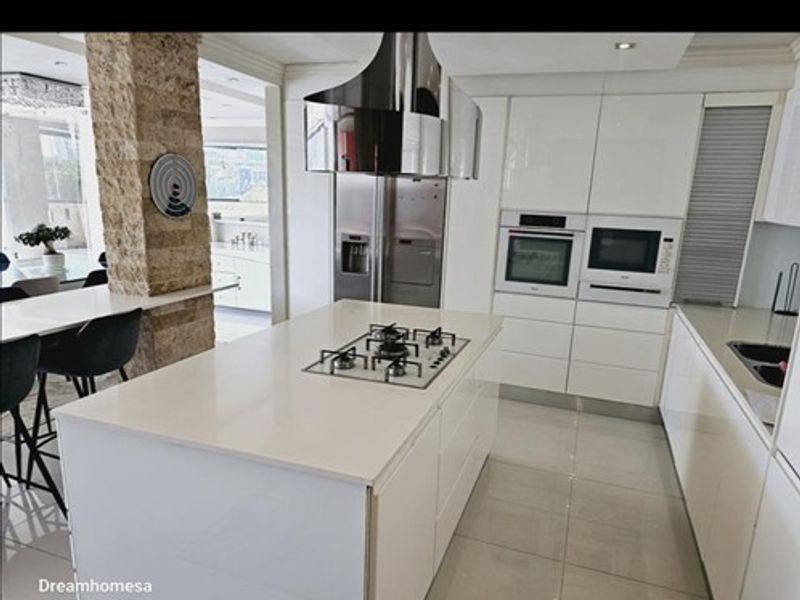 Modern kitchen featuring a central island with gas hob, high-gloss cabinetry, built-in appliances, and a distinctive stone-clad structural pillar.