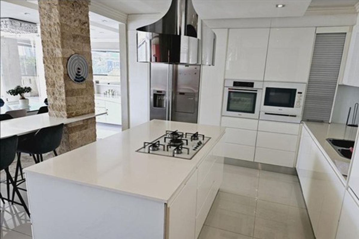 Modern kitchen featuring a central island with gas hob, high-gloss cabinetry, built-in appliances, and a distinctive stone-clad structural pillar.