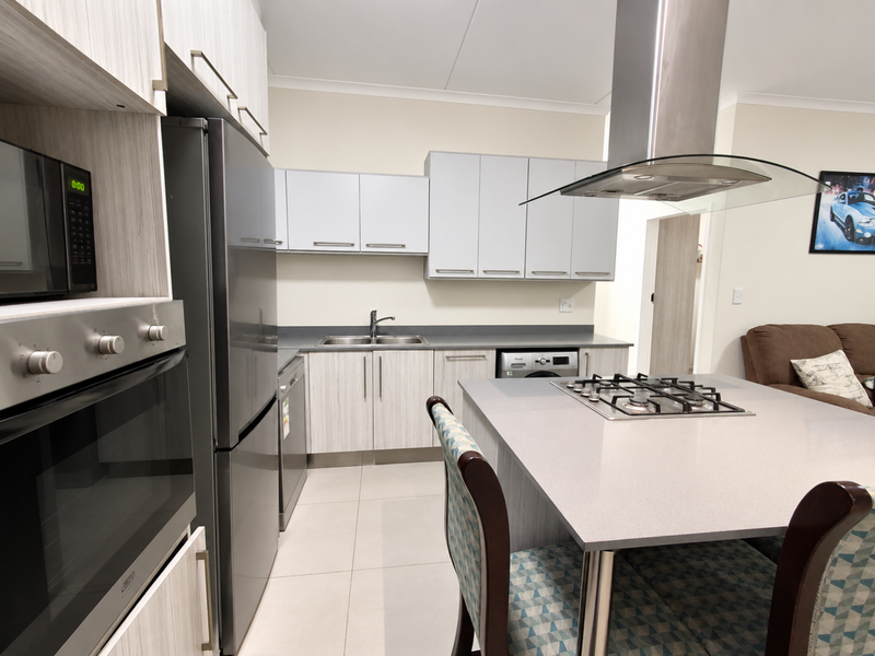 Modern kitchen featuring light wood-grain cabinetry, a central island with a gas hob, stainless steel appliances, and tiled flooring.