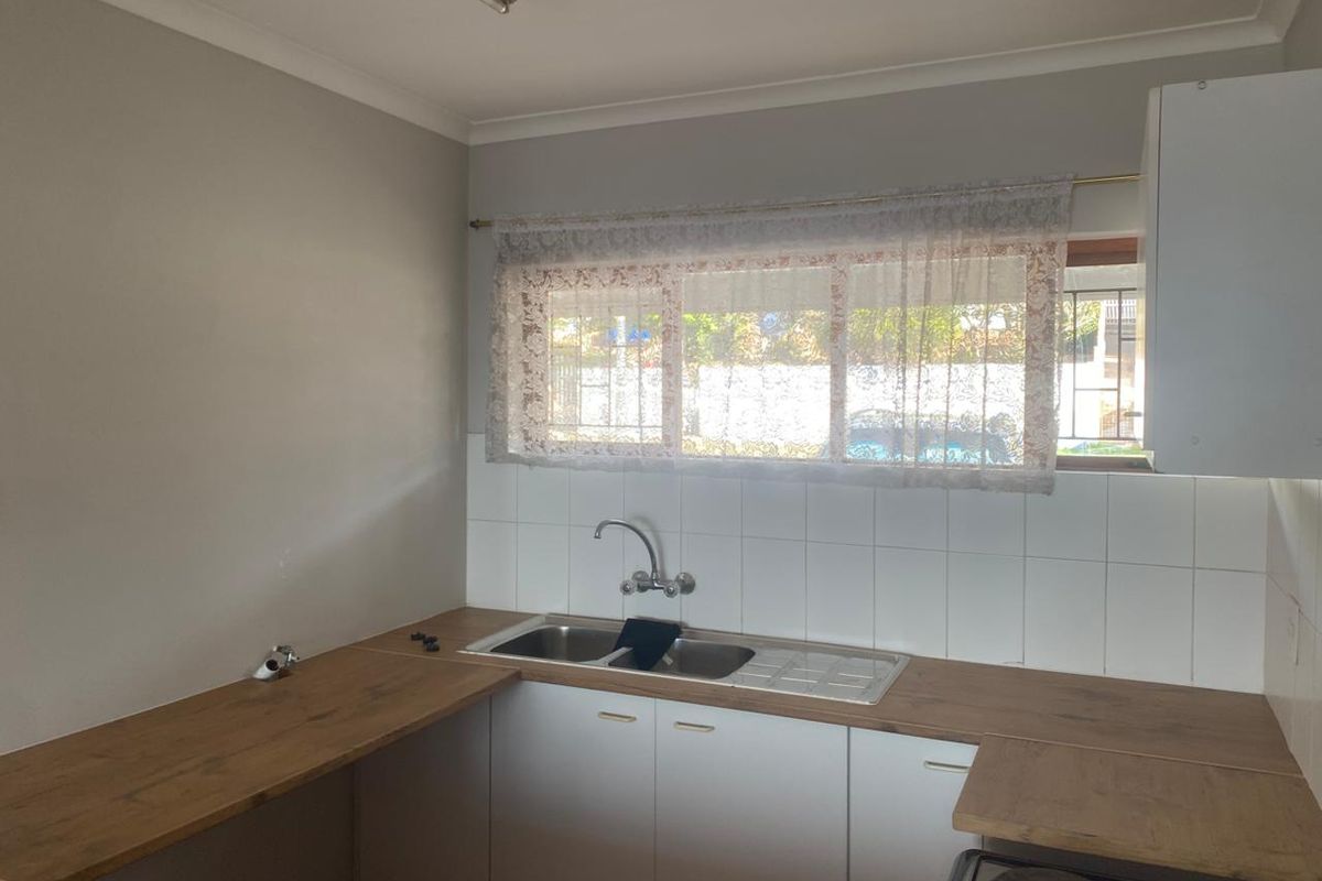A functional kitchen featuring white cabinetry, wood-look laminate countertops, a double bowl stainless steel sink, and a tiled splashback.