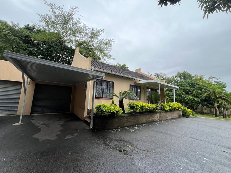 Front elevation of the townhouse featuring a carport, attached garage, and a paved driveway with a low retaining wall and established garden beds.