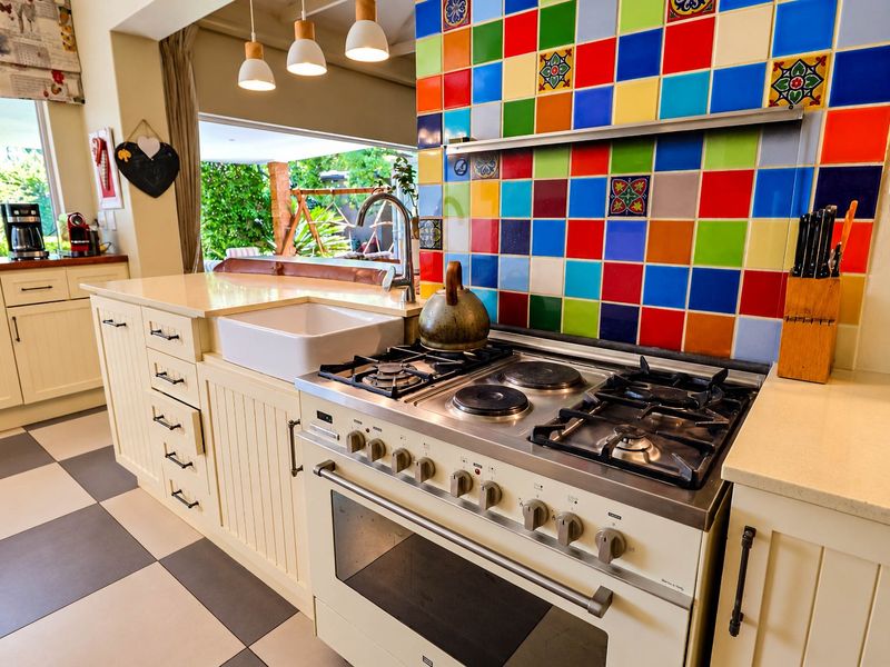A vibrant kitchen featuring a multi-colored tiled splashback, a large apron sink, stone countertops, and a professional-style gas and electric range cooker.