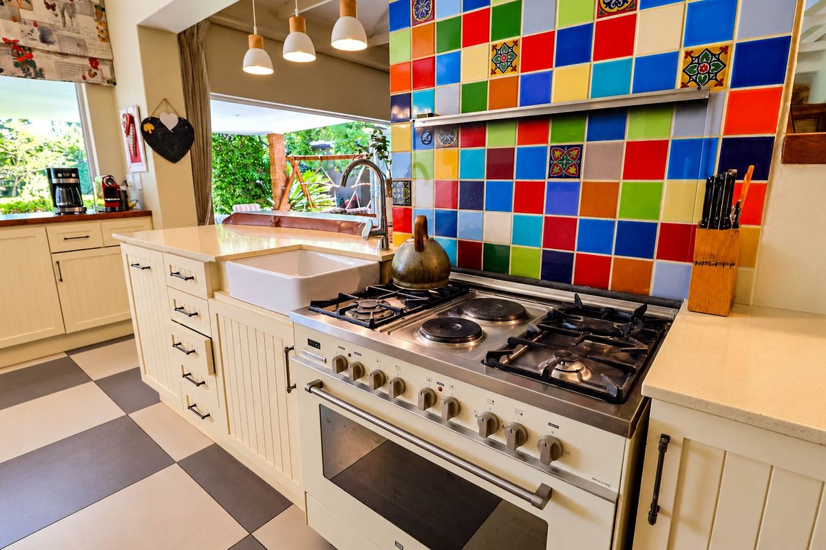 A vibrant kitchen featuring a multi-colored tiled splashback, a large apron sink, stone countertops, and a professional-style gas and electric range cooker.