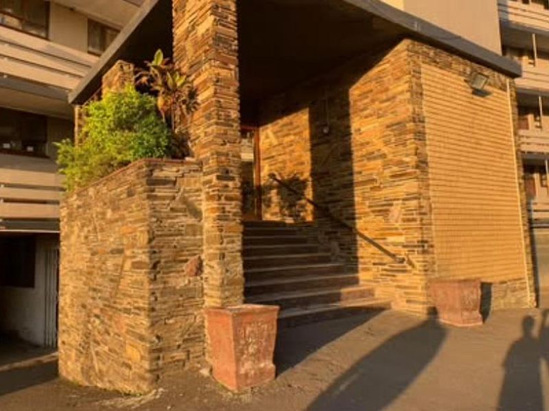 The apartment building entrance features stone-clad pillars, concrete stairs with a metal handrail, and exterior lighting, showing signs of age and weathering.