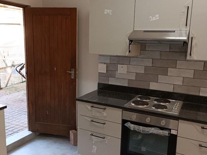 A modern, newly installed kitchen featuring sleek cabinetry, granite countertops, a built-in oven, and a stylish tiled backsplash with direct access to the exterior.