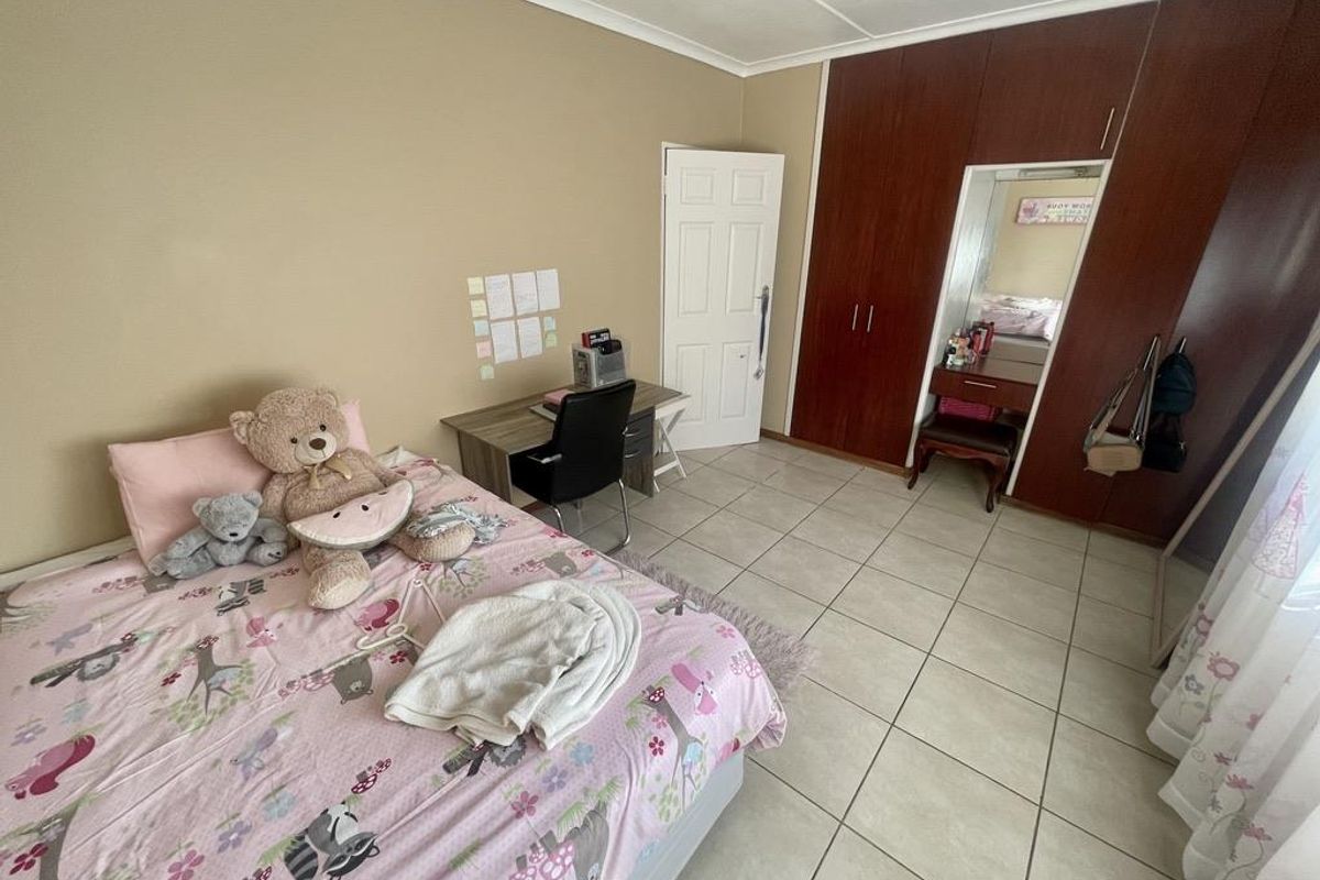 A bedroom featuring built-in wooden cupboards with an integrated vanity mirror and tiled flooring.