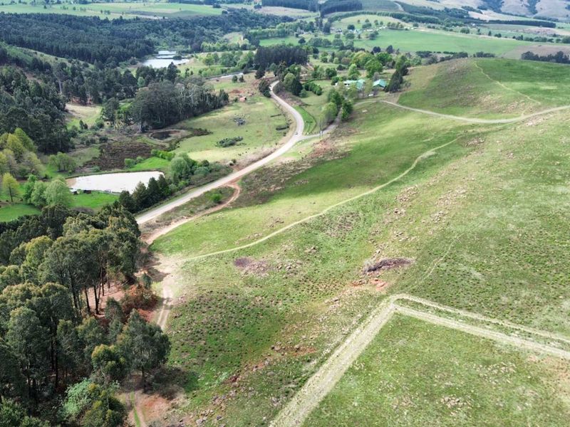 Aerial view of a large, undeveloped residential land parcel featuring rolling green hills, natural vegetation, and an existing dirt access track.