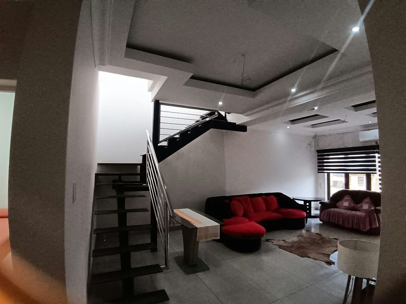Spacious living area featuring a modern staircase with stainless steel balustrade, recessed ceiling lighting, and tiled floors.
