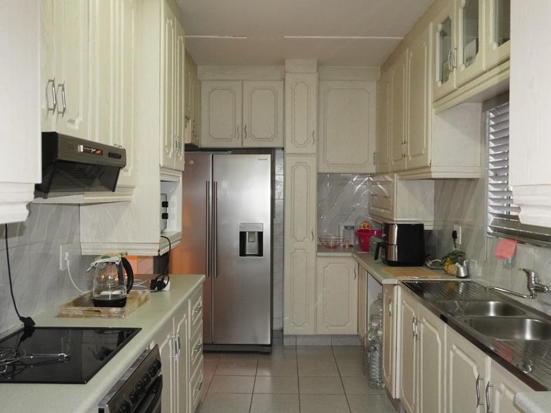 A functional galley-style kitchen featuring ample built-in cabinetry, a tiled backsplash, an electric hob, and a double sink with stainless steel fixtures.