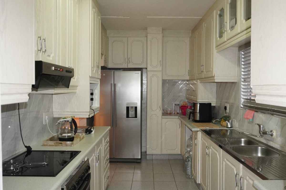 A functional galley-style kitchen featuring ample built-in cabinetry, a tiled backsplash, an electric hob, and a double sink with stainless steel fixtures.