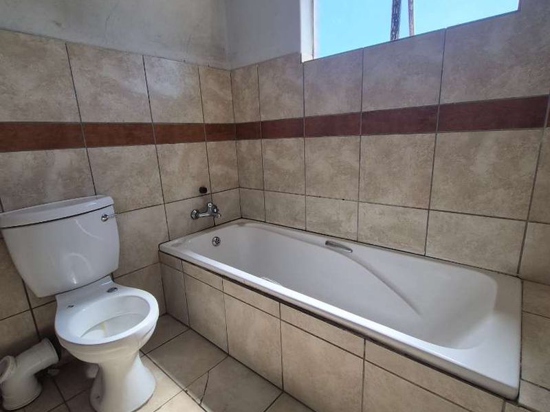 A functional bathroom featuring a bathtub and toilet with tiled finishes, currently requiring some cosmetic attention to the wall plastering and floor tiles.