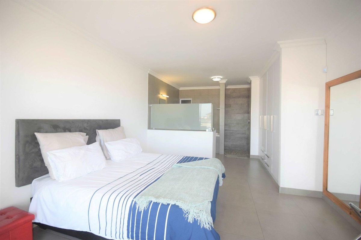 Spacious bedroom featuring an open-plan layout with an integrated en-suite bathroom, built-in wardrobes, and neutral tiled flooring.