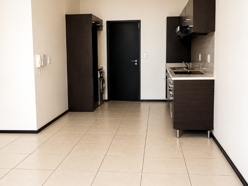 A clean, modern kitchen featuring dark wood cabinetry, integrated appliances, and neutral tiled flooring in an open-plan layout.