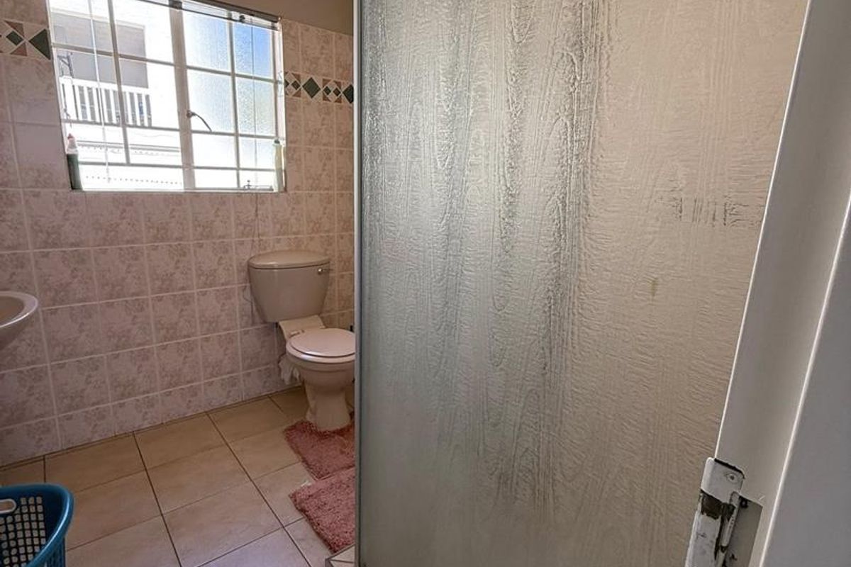 A functional bathroom featuring a shower enclosure, toilet, and tiled flooring, offering a dated aesthetic ready for modernization.