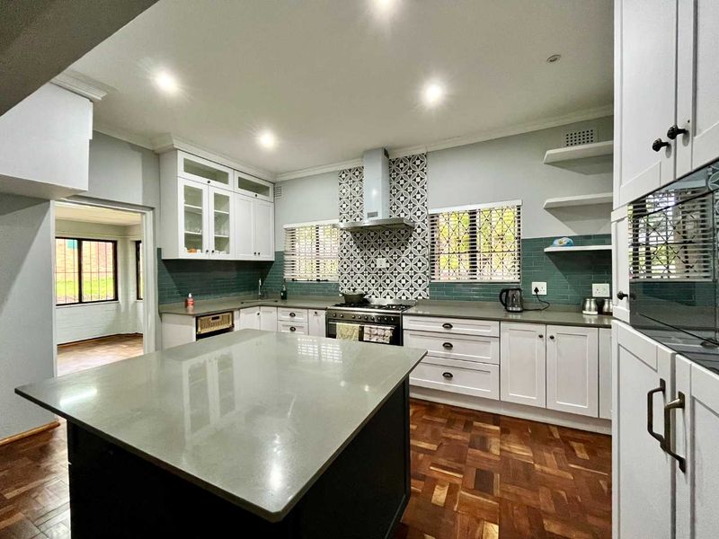 Modern kitchen featuring a central island, stone countertops, gas hob with extractor, stylish tiled backsplash, and warm parquet flooring.