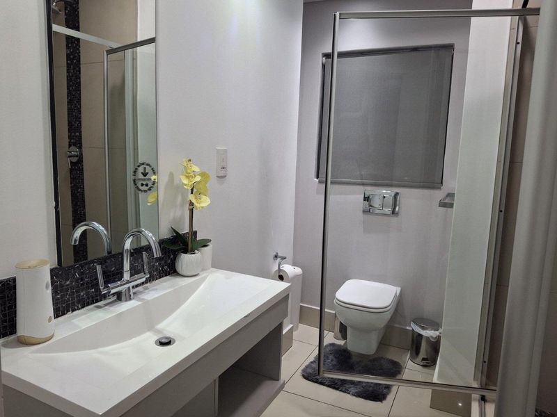Modern bathroom featuring a wall-mounted vanity with basin, wall-hung toilet with concealed cistern, and a glass-enclosed shower area.