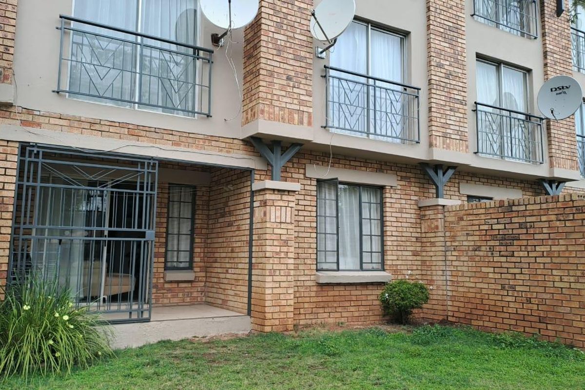 Exterior view of a multi-story brick apartment building featuring ground-level patio access, metal security gates, and upper-level balconies with railings.