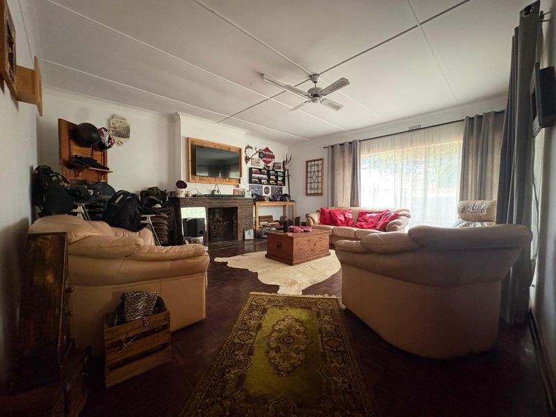 Spacious living room featuring classic parquet flooring, a brick fireplace, and a ceiling fan, offering a comfortable and traditional living space.
