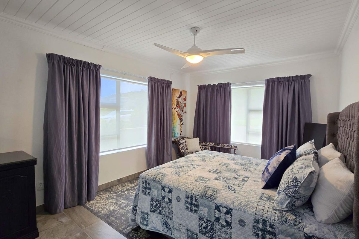 A well-lit bedroom featuring a white tongue-and-groove ceiling, a modern ceiling fan, and large windows with neutral flooring.