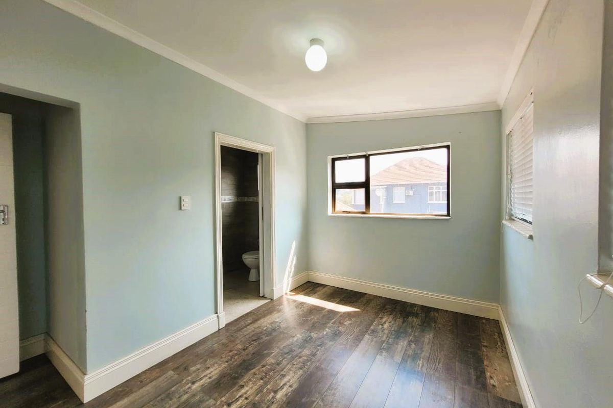 A bright, empty bedroom featuring wood-look laminate flooring, crown molding, and an adjoining en-suite bathroom.