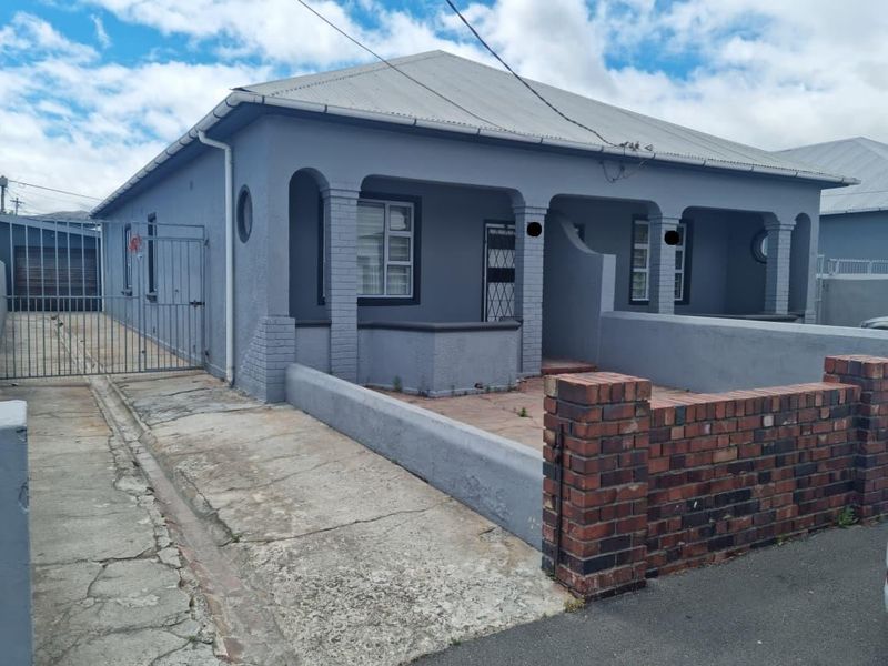Front elevation of a cluster home featuring a covered porch, brick boundary wall, metal driveway gate, and a corrugated metal roof.