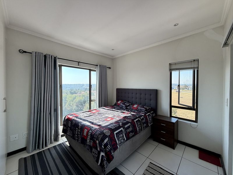 A bright bedroom featuring tiled flooring, recessed lighting, and large windows providing natural light and scenic views.