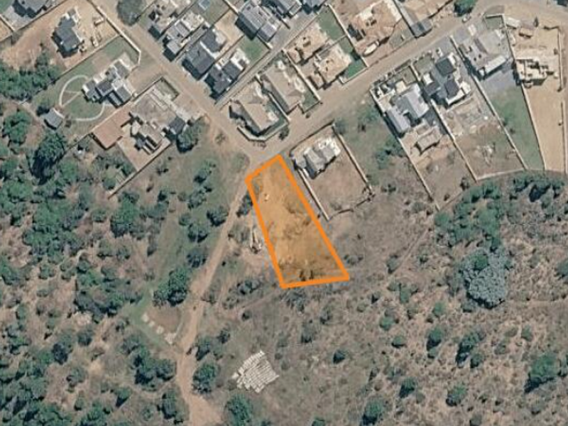 Aerial view of a vacant residential land plot situated in a developed neighborhood, highlighting the property boundaries and surrounding landscape.