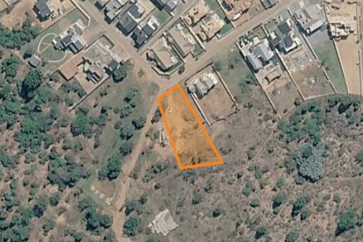 Aerial view of a vacant residential land plot situated in a developed neighborhood, highlighting the property boundaries and surrounding landscape.