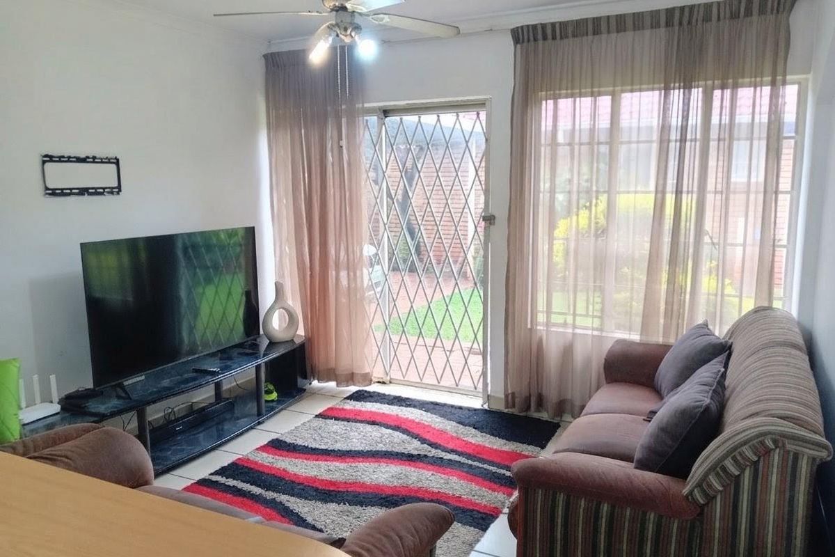 A living room featuring tiled flooring, a ceiling fan, and a security gate leading to the exterior.