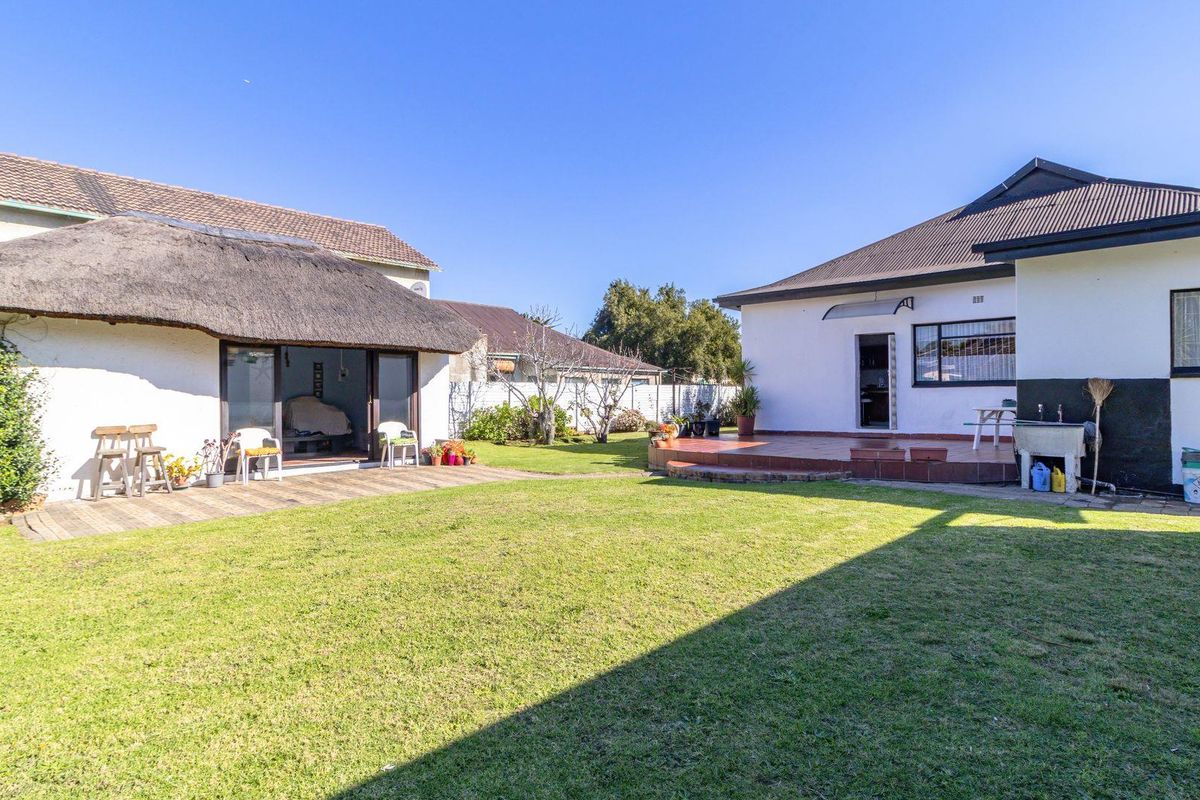 Spacious rear garden featuring a lawn area, a thatched-roof structure, and a paved patio area attached to the main residence.