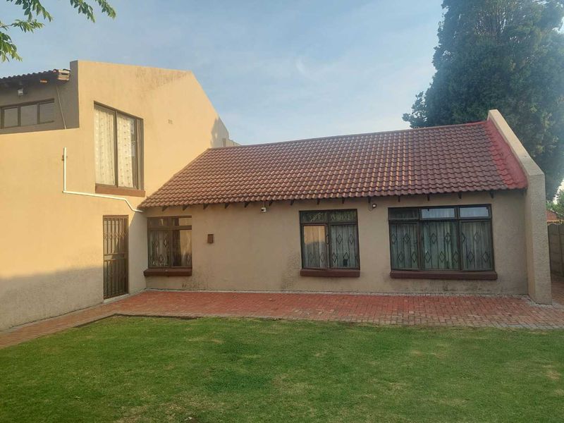 Rear view of the house featuring a paved patio area, lawn, and traditional tiled roof architecture.