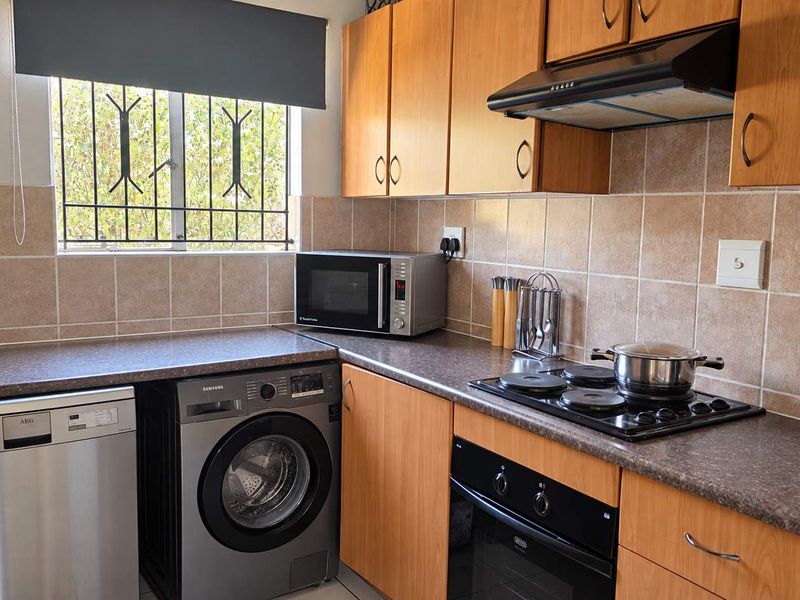 Functional kitchen featuring wood-look cabinetry, tiled backsplash, built-in oven, electric hob, extractor fan, and integrated space for laundry appliances.