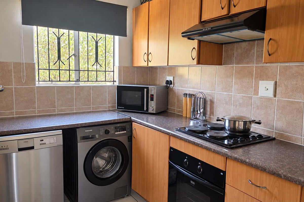 Functional kitchen featuring wood-look cabinetry, tiled backsplash, built-in oven, electric hob, extractor fan, and integrated space for laundry appliances.