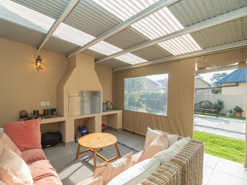 Covered patio area featuring a built-in braai, tiled flooring, and protective outdoor canvas blinds, overlooking the rear garden.