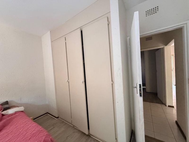 A bedroom featuring built-in cupboards and access to a tiled hallway, showing standard wear and tear on finishes.