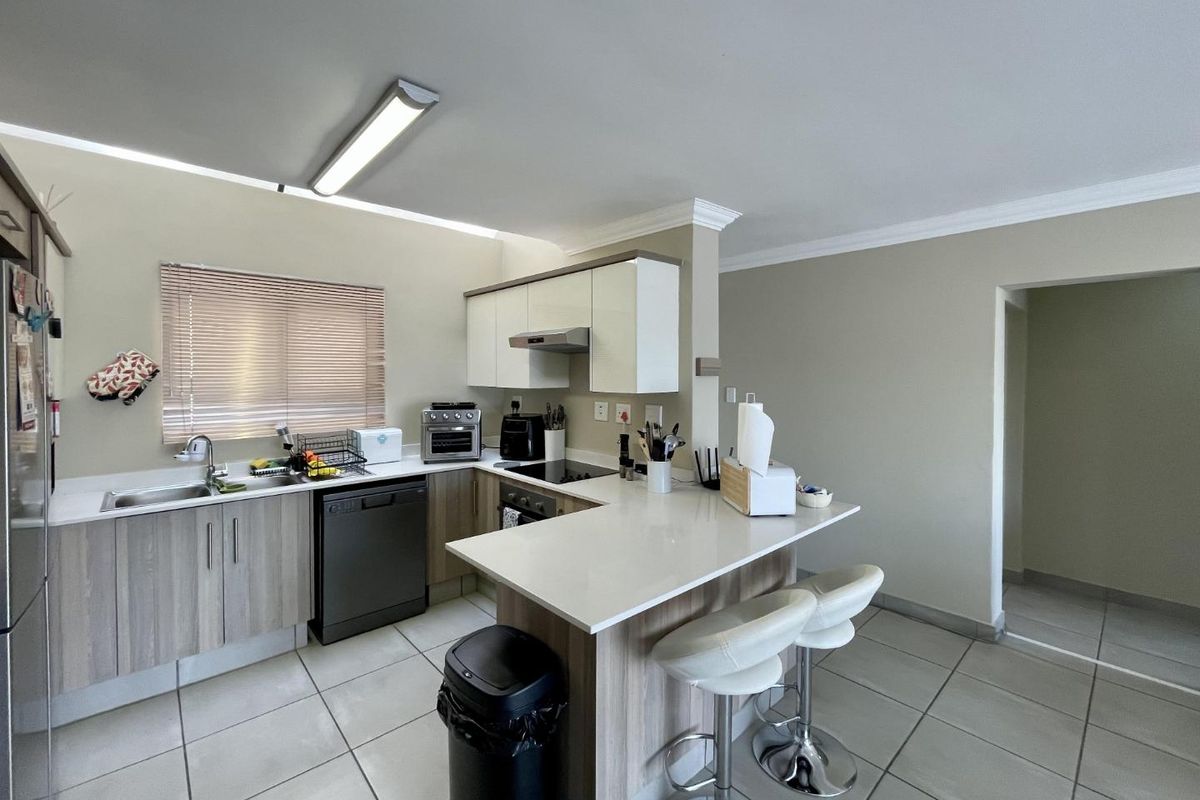 Modern kitchen featuring light wood-grain cabinetry, quartz countertops, a breakfast bar, and integrated appliances, finished with neutral tiled flooring.