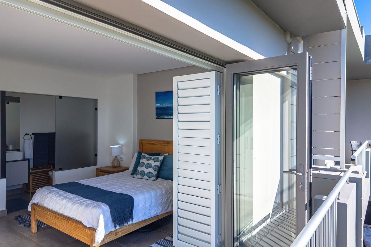 Modern bedroom featuring large glass sliding doors that open onto a private balcony, with an integrated en-suite bathroom visible.