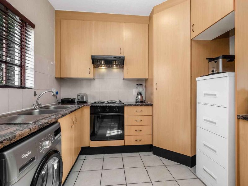 Compact kitchen featuring light wood cabinetry, granite countertops, built-in oven, electric hob, and tiled flooring with integrated laundry plumbing.