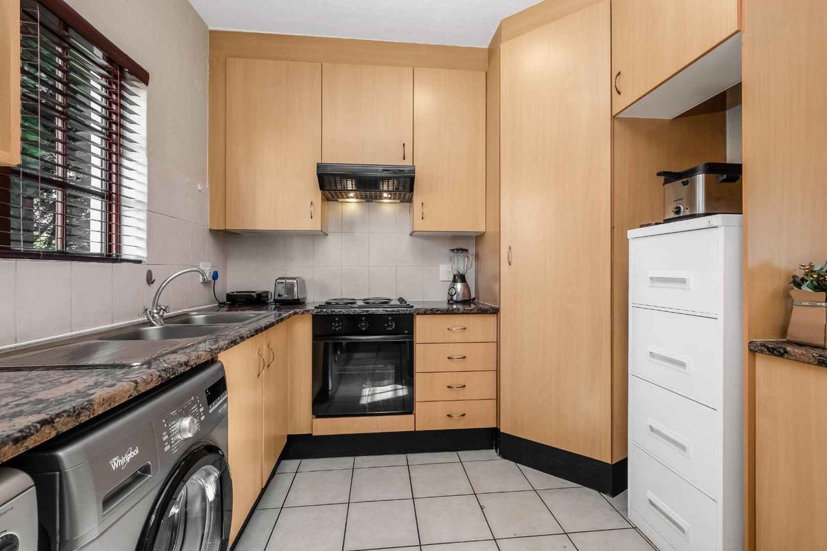 Compact kitchen featuring light wood cabinetry, granite countertops, built-in oven, electric hob, and tiled flooring with integrated laundry plumbing.