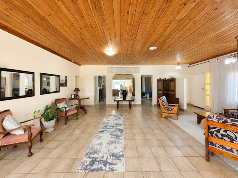 Spacious living area featuring a warm timber tongue and groove ceiling, neutral ceramic floor tiles, and an open-plan layout with an inviting archway.