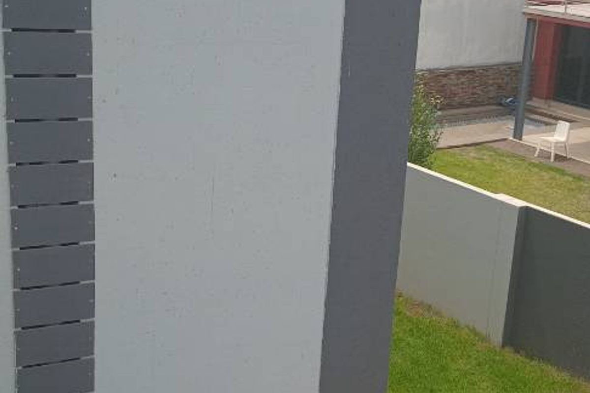 A view of the side exterior area featuring paved ground, a modern wall structure with decorative slats, and a glimpse of the rear garden.