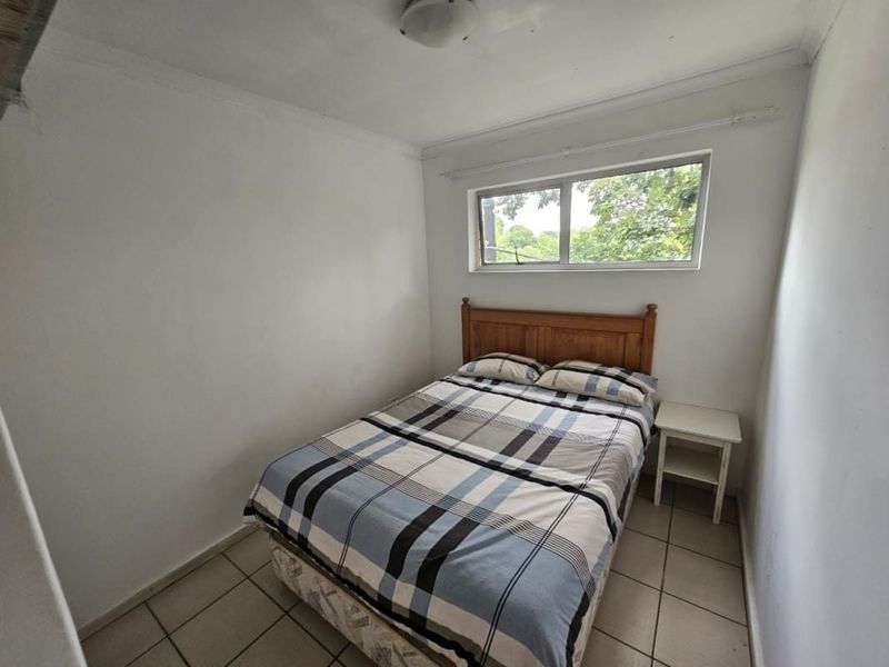 A compact bedroom featuring tiled flooring and a window providing natural light.