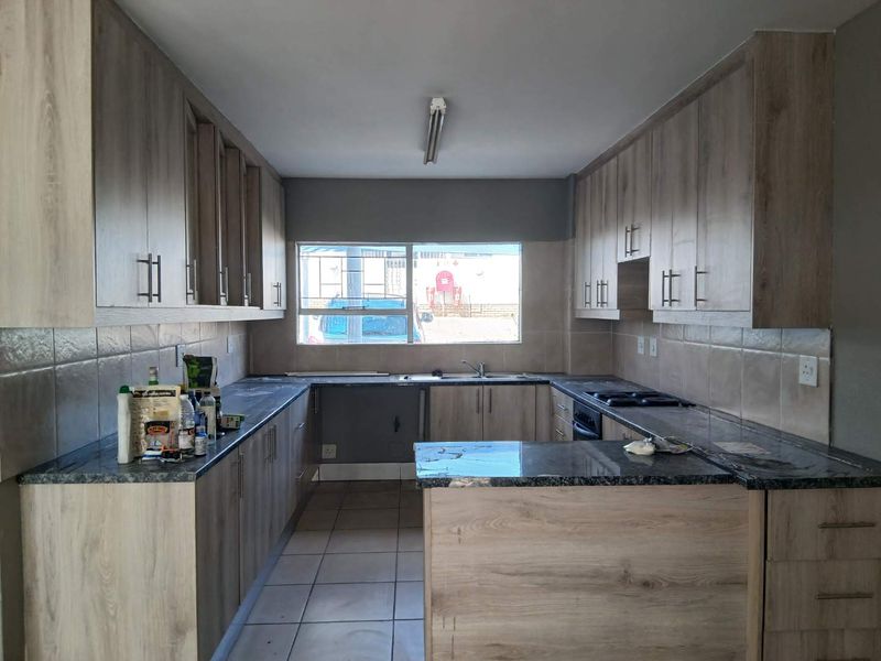 A functional kitchen featuring light wood-look laminate cabinetry, dark granite countertops, a built-in hob and oven, and neutral tiled flooring.