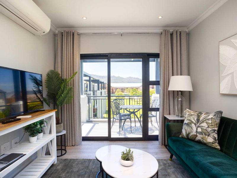 A well-maintained living room featuring modern laminate flooring, recessed lighting, a split-system air conditioner, and a sliding glass door leading to a balcony.