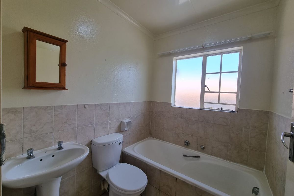 A functional bathroom featuring a pedestal basin, toilet, and bathtub with tiled splashbacks and a window providing natural light.