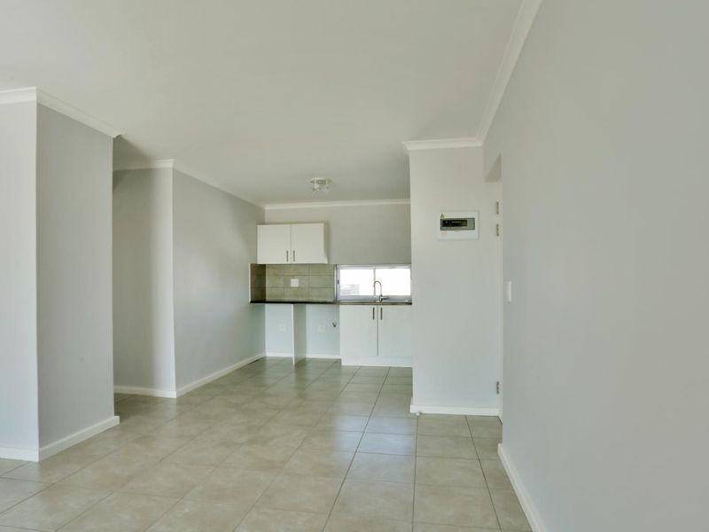 An open-plan living and kitchen area featuring neutral tiled flooring, clean white walls, and functional built-in kitchen cabinetry.