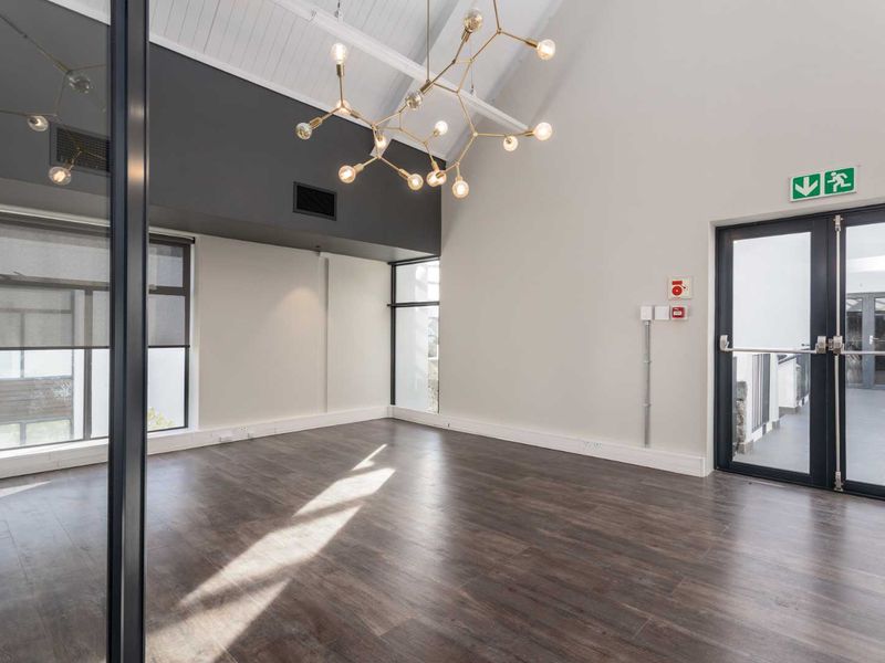 Modern, bright office space featuring vaulted ceilings with exposed rafters, dark laminate flooring, and a glass partition wall, offering a professional and airy atmosphere.