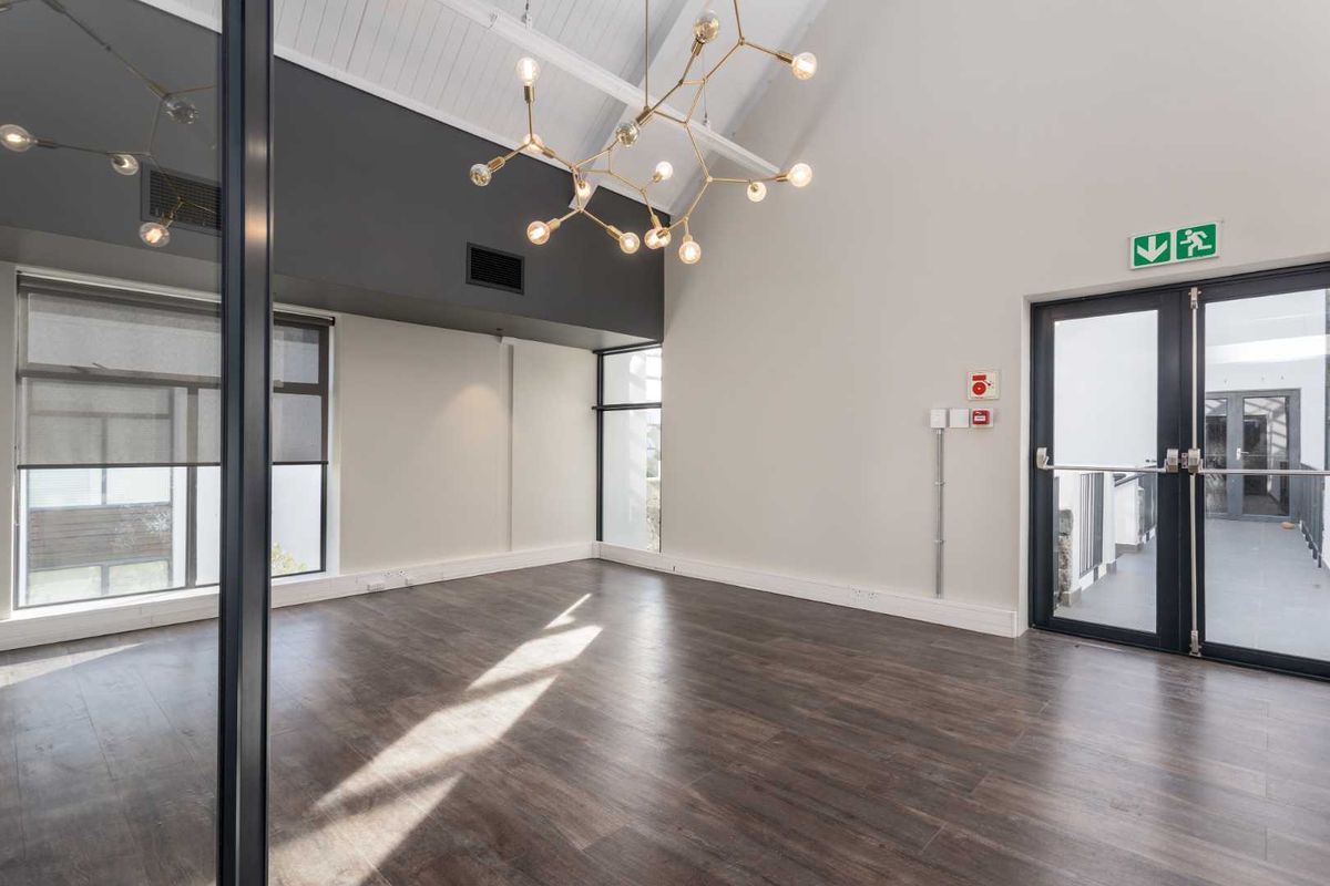 Modern, bright office space featuring vaulted ceilings with exposed rafters, dark laminate flooring, and a glass partition wall, offering a professional and airy atmosphere.